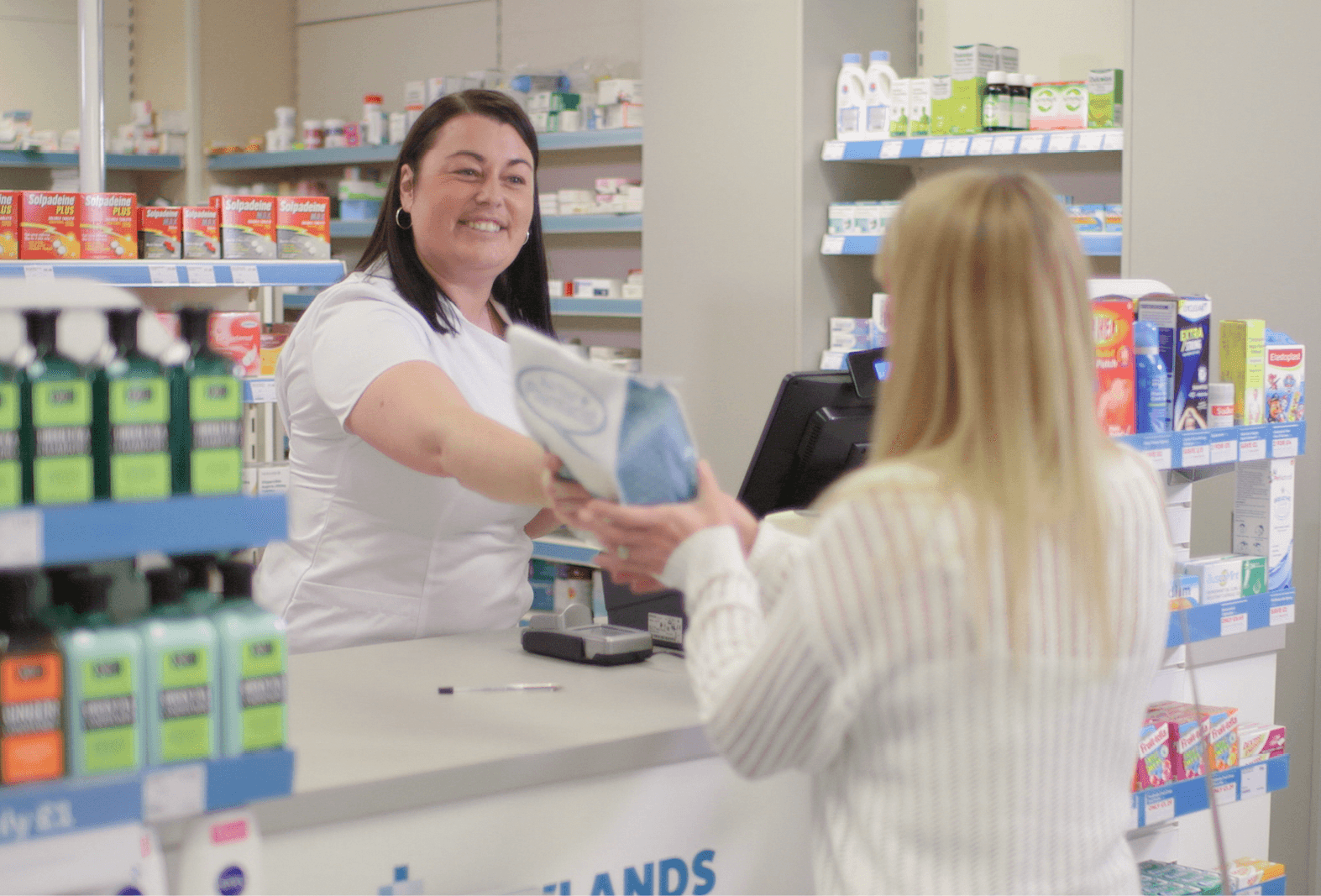 happy pharmacy team member handing over meds in discreet way