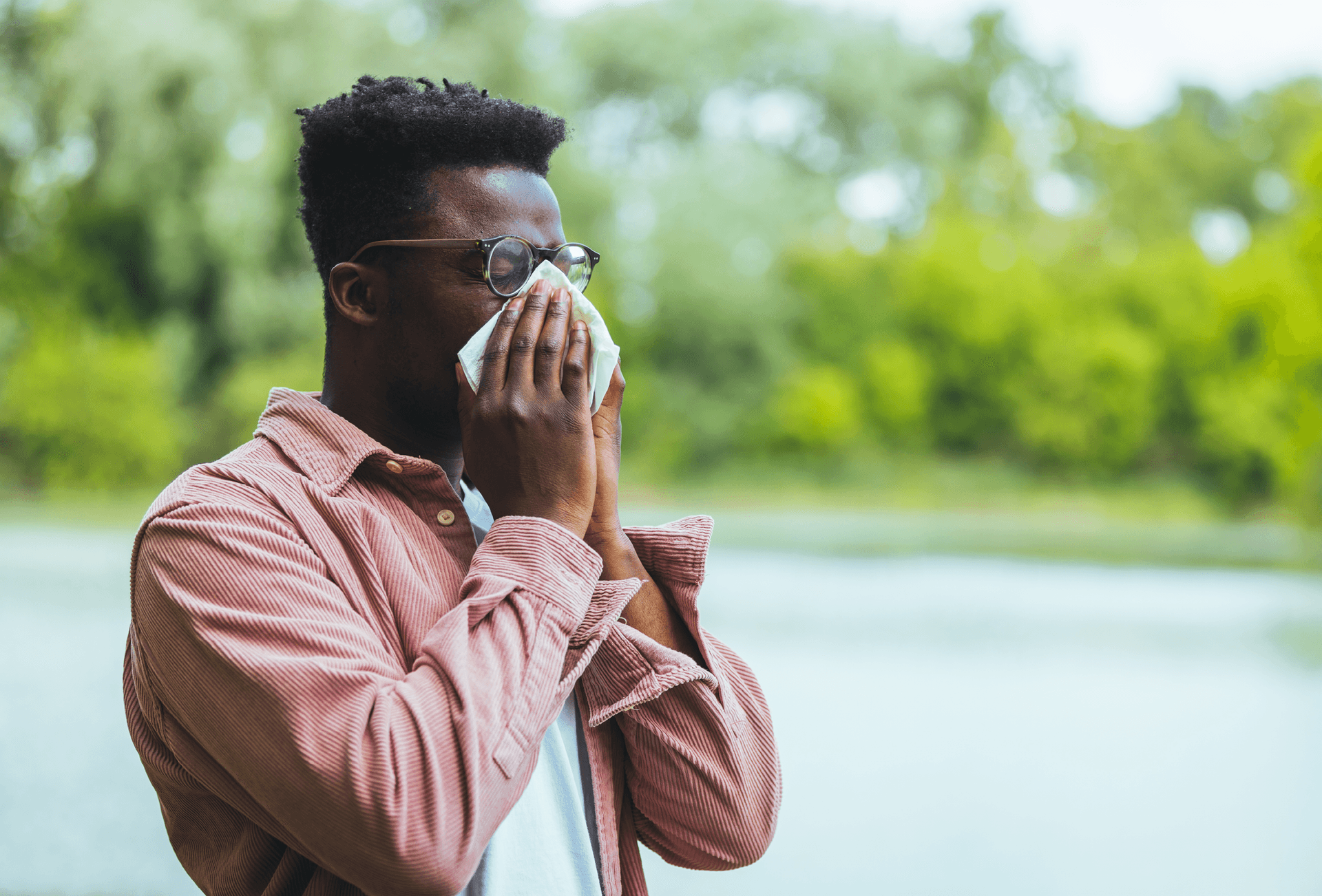 man blowing nose near trees and shrubs