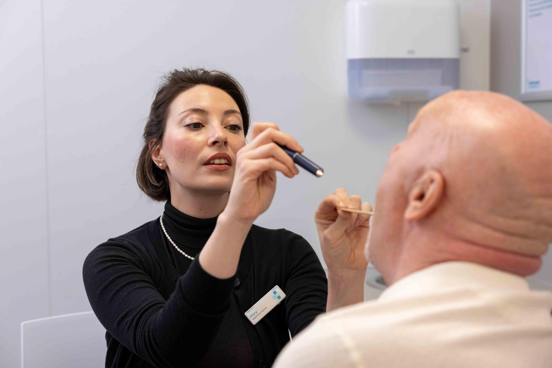 Female pharmacist checking a male patient's throat with a torch