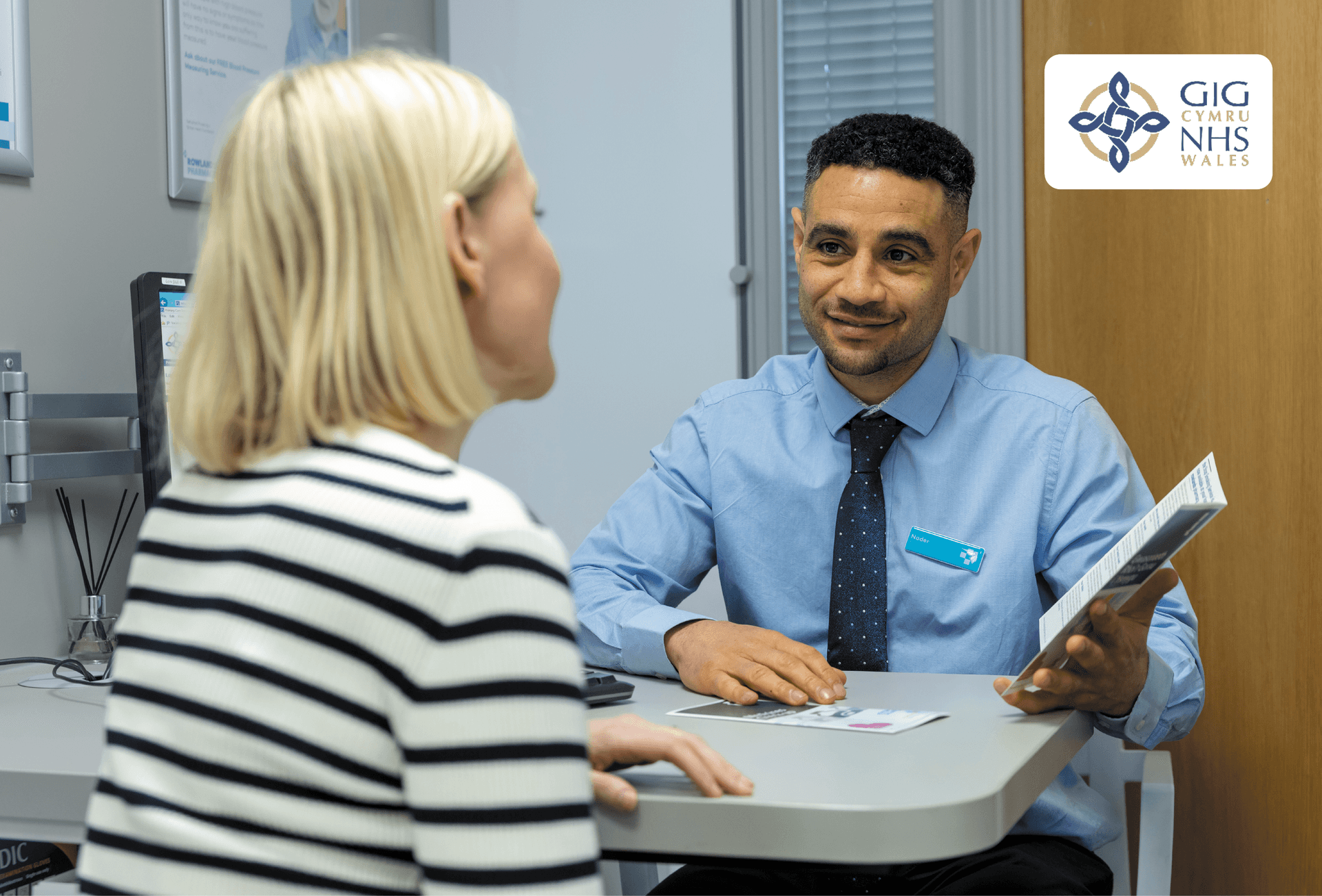 pharmacist giving advice to customer with NHS Wales logo