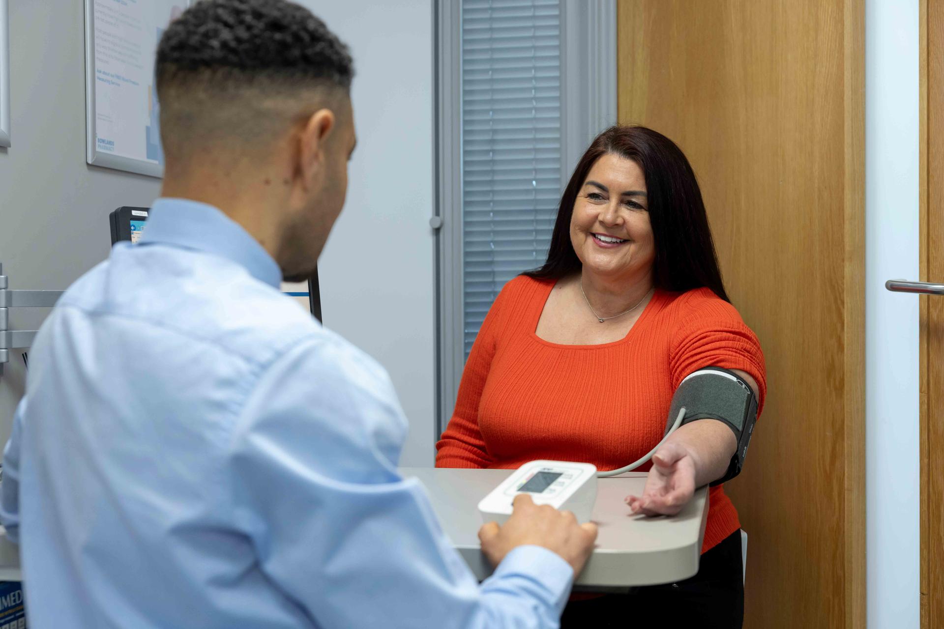 Male pharmacist using a blood pressure pump on a female patient in a private consultation room