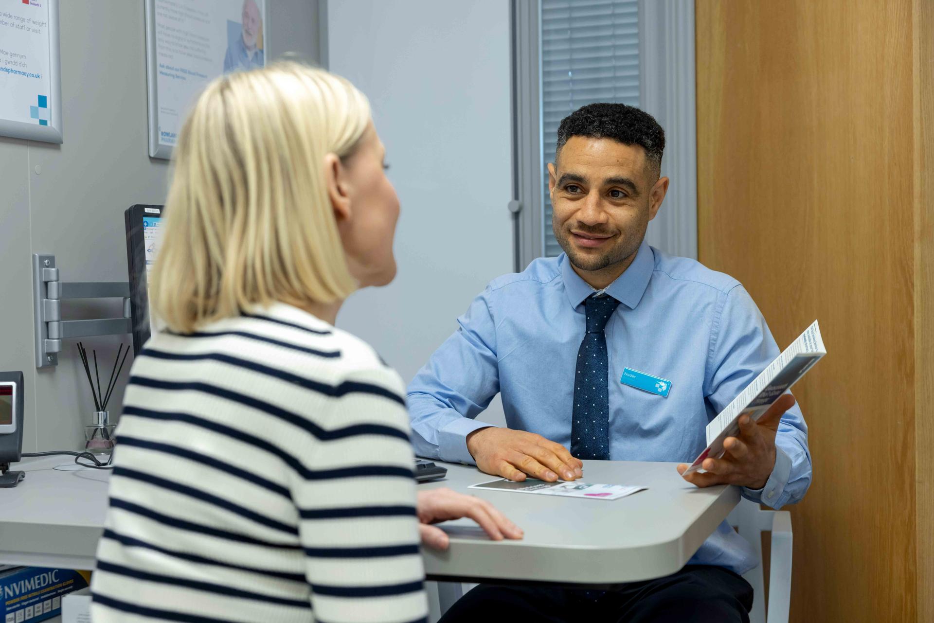 Male pharmacist speaking to a female patient in a private consultation room