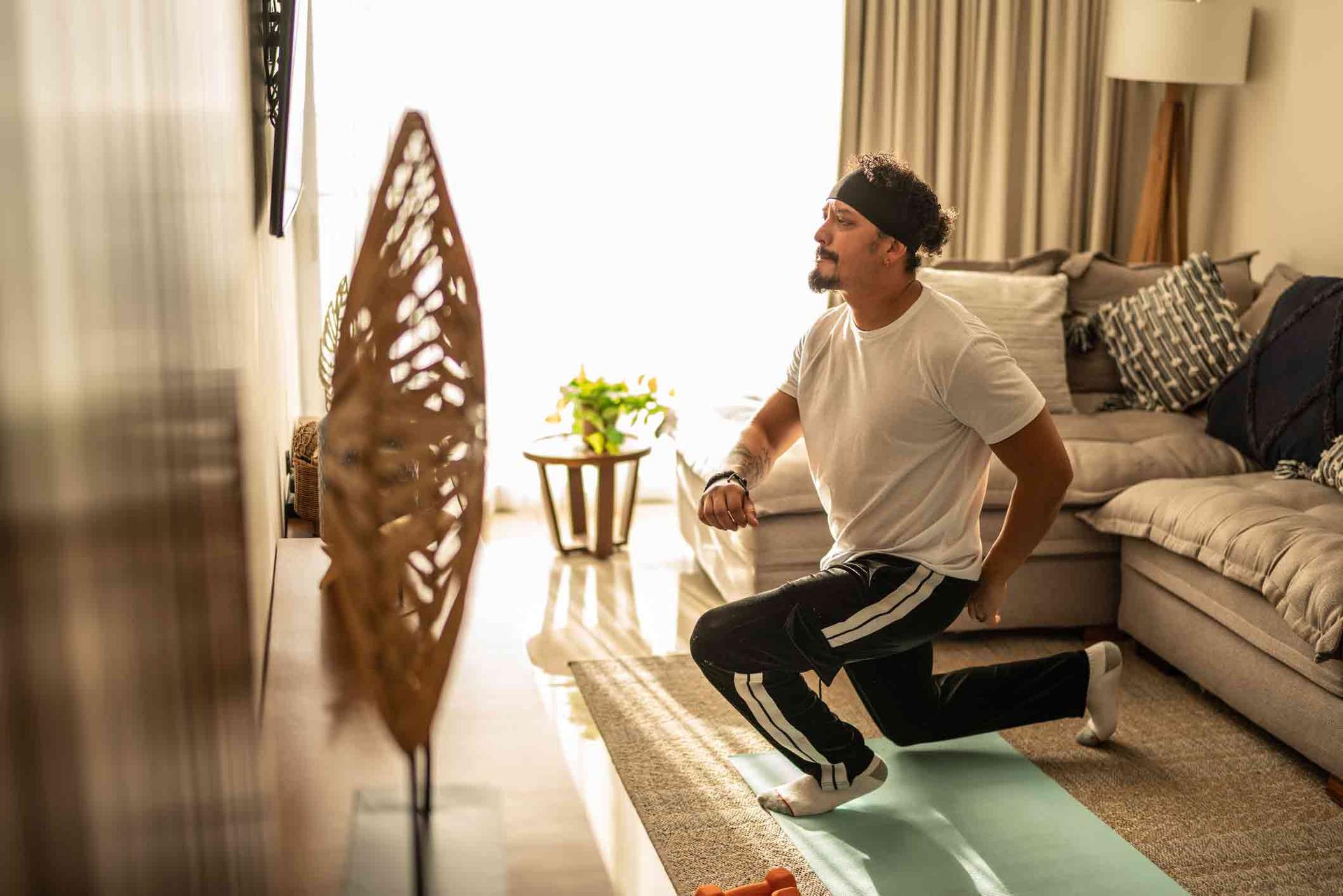 A man exercising in his living room whilst watching the television