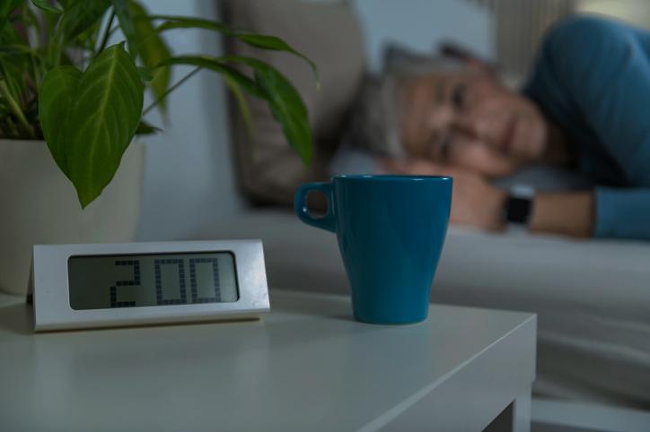 Lady lying away in bed looking at a coffee mug on the bedside table